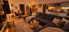 A modern living room with a dark-colored sectional sofa, a round coffee table, and a dining area with a small table and chairs. - New Listing (Lünen)