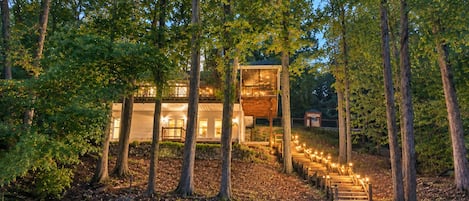 A wooden structure with a staircase leading to a deck, surrounded by trees and a stone pathway.
