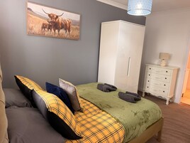 Un dormitorio con cama, almohadas, un armario, una lámpara y un cuadro en la pared.