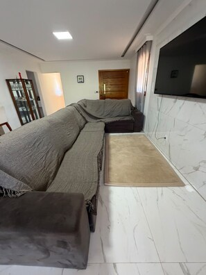 A room with a sofa, a television mounted on the wall, a wooden door, and a marble floor. - New Listing (Batatuba)