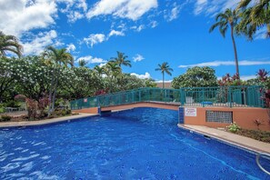 A swimming pool with a green bridge, surrounded by palm trees and tropical plants. - Family-Friendly 4-Bedroom Retreat – Steps to the Pool & Across from the Ocean! (Kihei)