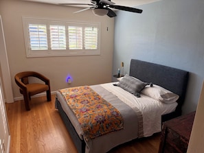 A bedroom with a bed, a chair, a nightstand, and a ceiling fan. - Modern Kitchen 3BR Home w/ Yard (San Luis Obispo)