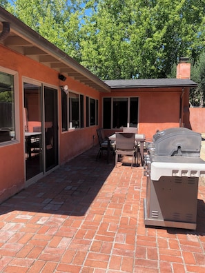 A patio area with a brick floor, a grill, a table with chairs, and a covered seating area. - Modern Kitchen 3BR Home w/ Yard (San Luis Obispo)