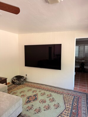 A living room with a flat-screen TV mounted on the wall, a patterned rug, and a sofa.
