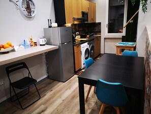 A compact kitchen with a refrigerator, microwave, and washing machine, a dining table with chairs, and a clock on the wall. - New Listing (Tonnarella)