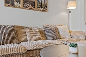Un salon moderne avec un canapé, plusieurs coussins, une table basse ronde, un lampadaire et une petite plante en pot.