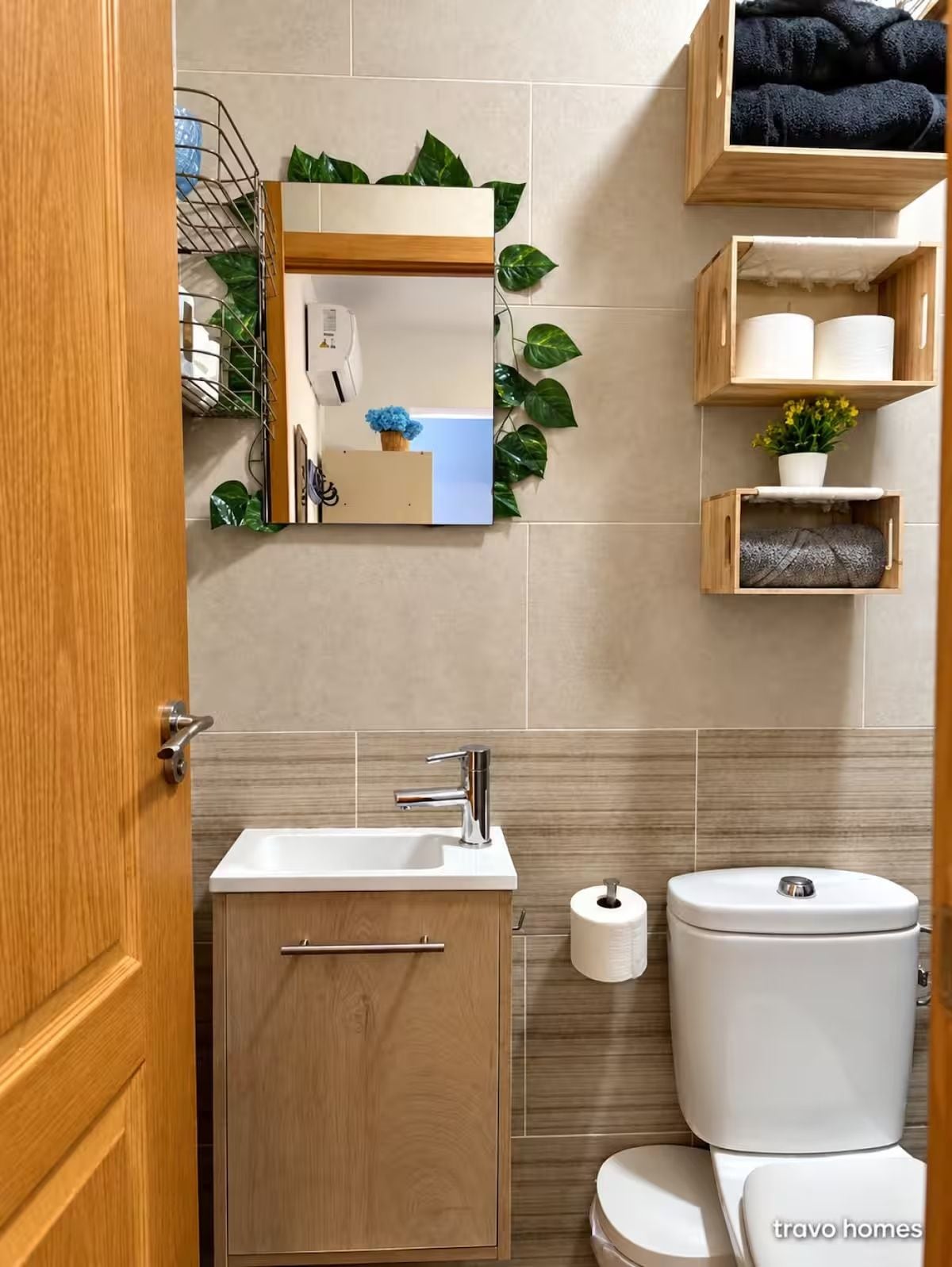 Et badeværelse med skab i træ, vask, toilet og et spejl med en plante.