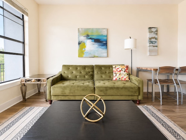 A living room with a green sofa, a coffee table, and a painting on the wall. - Sleepover | Beautiful 1BD/1BA+ Riverfront View LIT (North Little Rock)