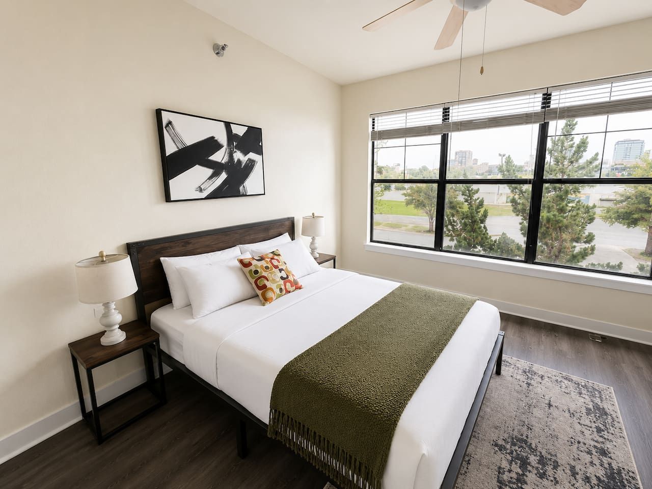 A hotel room with a large bed, a nightstand, a lamp, a window with a view, and a ceiling fan.