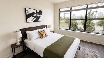 A hotel room with a large bed, a nightstand, a lamp, a window with a view, and a ceiling fan.
