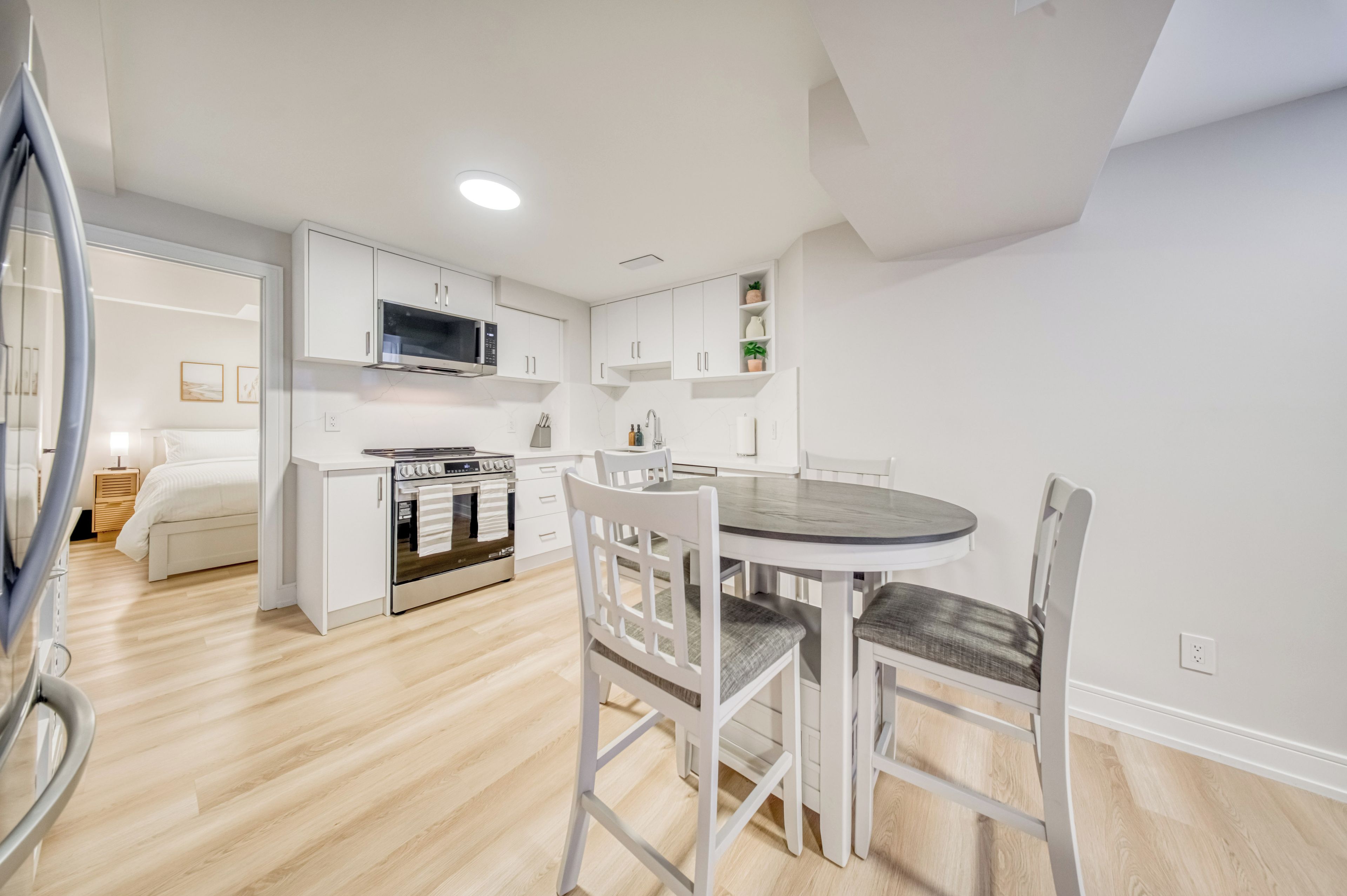 A modern kitchen with white cabinetry, a built-in microwave, and a dining area with a round table and white chairs.