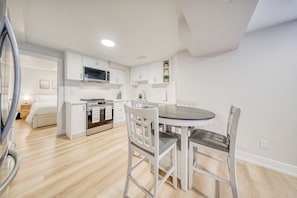 Una cocina moderna con armarios blancos, microondas integrado y comedor con mesa redonda y sillas blancas.