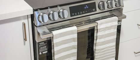 A stainless steel kitchen with a built-in oven and stovetop, featuring control knobs and a digital display.