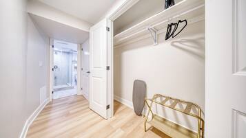 A hallway with a wooden floor, a door leading to a bathroom, and a wall-mounted ironing board with hangers.