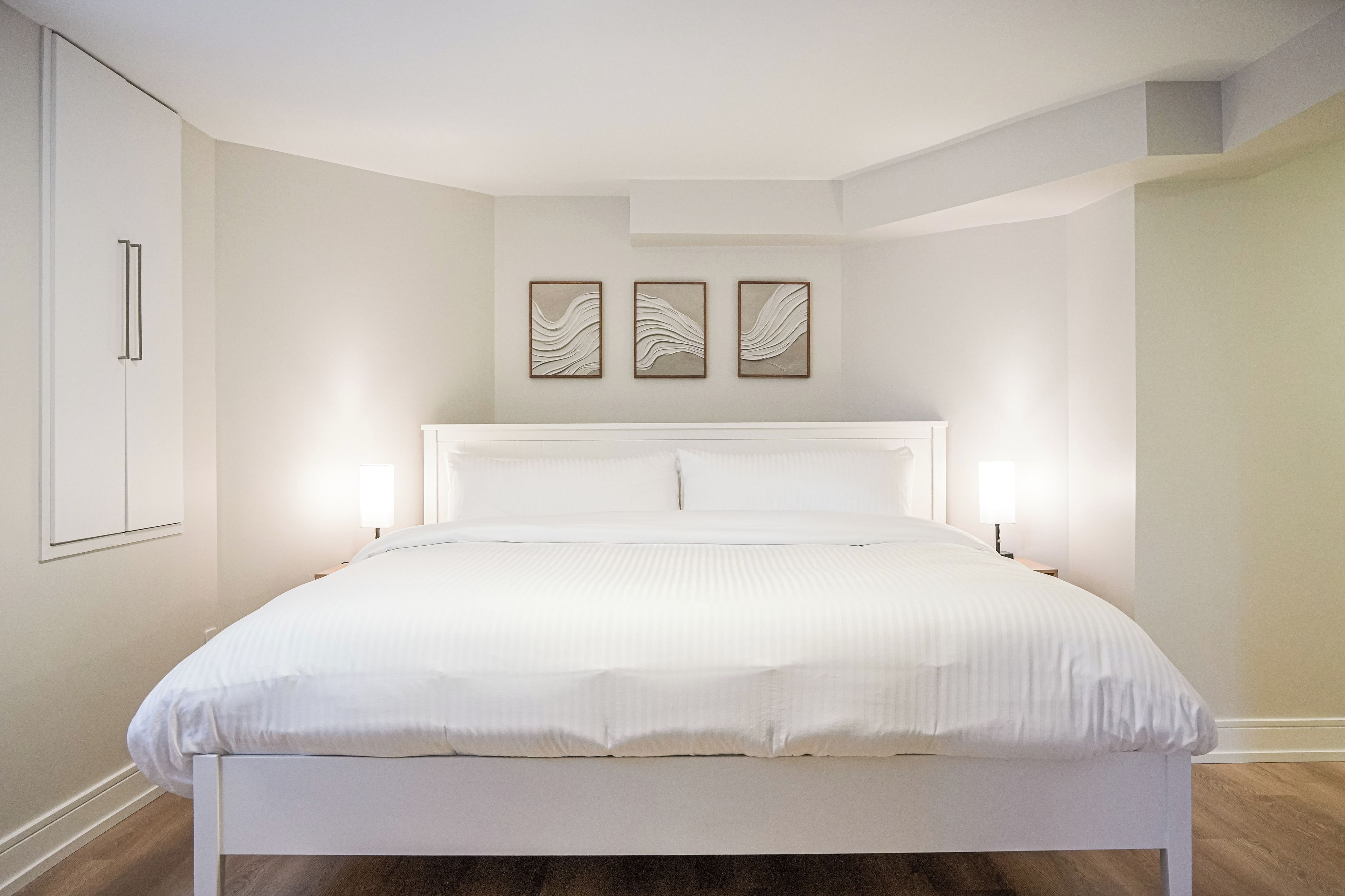 Une chambre à coucher avec un grand lit, deux tables de chevet, une armoire et trois œuvres d’art accrochées au mur.