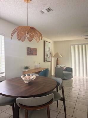 A dining area with a round wooden table, two chairs, a woven pendant light, and a wall-mounted air vent. - Welcome to the Sandy Beach Oasis, your relaxing New Smyrna Beach getaway! (New Smyrna Beach)