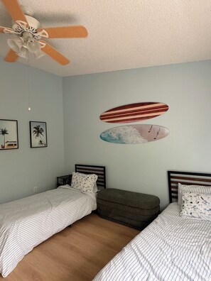 A bedroom with two single beds, a ceiling fan, and a surfboard mural on the wall. - Welcome to the Sandy Beach Oasis, your relaxing New Smyrna Beach getaway! (New Smyrna Beach)