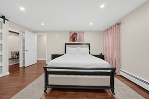 A bedroom with a bed, nightstands, a painting, and a door leading to another room. - Spacious 4BR Home Near Binghamton & UHS (Endicott)
