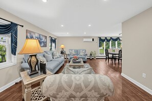 Ein geräumiges Wohnzimmer mit einer Couch, Sesseln, einem Couchtisch und einem Essbereich mit Tisch und Stühlen.