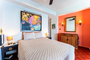 A hotel room with a bed, a nightstand, a dresser, a painting, and a mirror. - Cozy oceanfront studio (Puerto Vallarta)