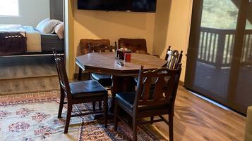 Un espace repas comprenant une grande table, des chaises, un téléviseur fixé au mur et une vue sur l’extérieur grâce à une porte coulissante.