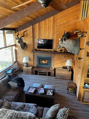 A cozy living room with a fireplace, mounted animal heads, a television, and a comfortable seating area. - Beautiful Large Wood Cabin with Large Covered Deck (Bradley)