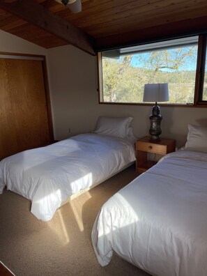 A room with two beds, a window with a view of trees, a wooden ceiling, and a nightstand with a lamp. - Beautiful Large Wood Cabin with Large Covered Deck (Bradley)