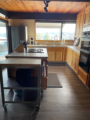A modern kitchen with a large island, wooden cabinets, and a view through the window.