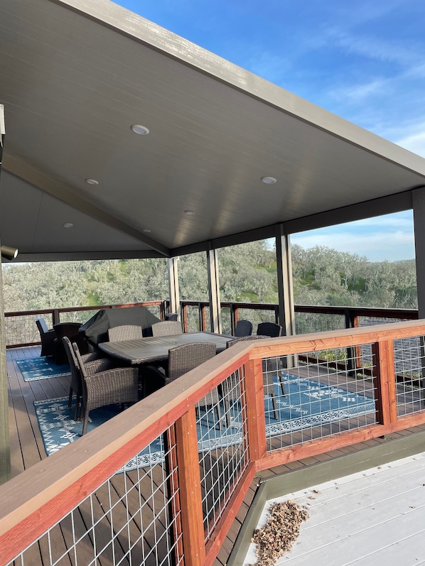 A covered outdoor deck with a pool, wicker furniture, and a view of trees.