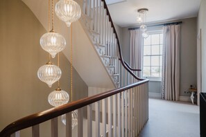 A staircase with a wooden handrail and a white railing, leading to a landing with a large window and a chandelier. - Beautiful Georgian Farmhouse Country Escape (Gloucester)