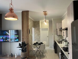 A modern kitchen with a dining area, a flat-screen TV, and a potted plant. - Cozy Retreat in Carlswald 229 (Johannesburg)