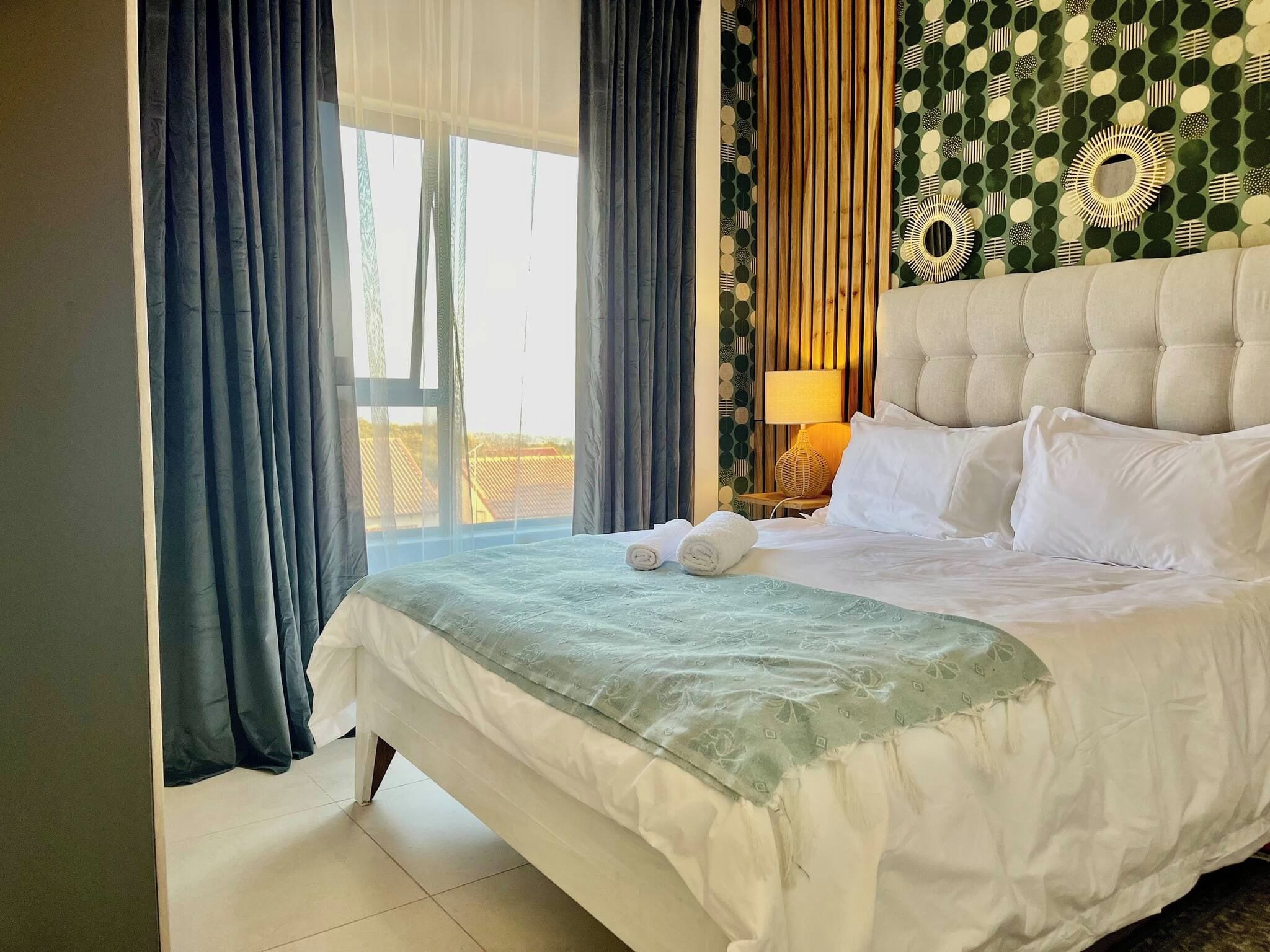 Une chambre d’hôtel avec un grand lit, une fenêtre avec des rideaux, un mur décoré d’un motif et une lampe de chevet.
