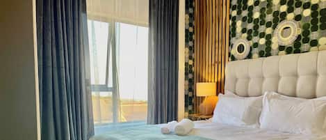 A hotel room with a large bed, a window with curtains, a patterned wall, and a bedside lamp.