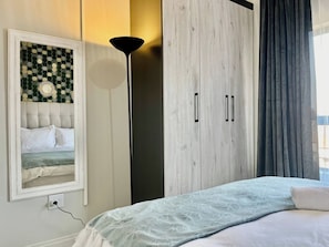 A bedroom with a bed, a wardrobe, a floor lamp, and a wall decoration. - Cozy Retreat in Carlswald 229 (Johannesburg)