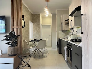 A modern kitchen with a dining area, featuring a built-in oven, a sink, and a countertop with a kettle. - Cozy Retreat in Carlswald 229 (Johannesburg)