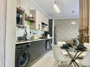 A modern kitchen with a washing machine, a dining area with a glass table, and pendant lighting. - Cozy Retreat in Carlswald 229 (Johannesburg)