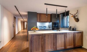 Une cuisine moderne avec des meubles en bois, un îlot central, des luminaires suspendus et une tête de cerf fixée au mur.
