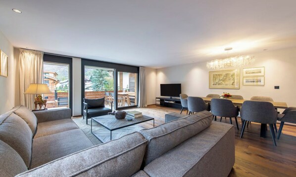 A modern living room with a sofa, coffee table, and dining area. - LUXURY ALPINE APARTMENT WITH SPA, TECHNOGYM & PRIVATE CINEMA (Zermatt)