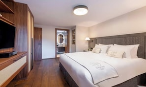 A hotel room with a large bed, a television, a wardrobe, and a bathroom visible through an open door. - LUXURY ALPINE APARTMENT WITH SPA, TECHNOGYM & PRIVATE CINEMA (Zermatt)