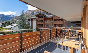 A balcony with wooden railings, outdoor seating, and a view of a mountain and buildings. - LUXURY ALPINE APARTMENT WITH SPA, TECHNOGYM & PRIVATE CINEMA (Zermatt)