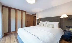Une chambre d’hôtel avec un grand lit, une armoire, une table de chevet avec une lampe et une petite table de nuit.