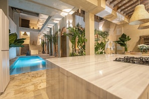 Um interior moderno com piscina, balcão de mármore e plantas tropicais.