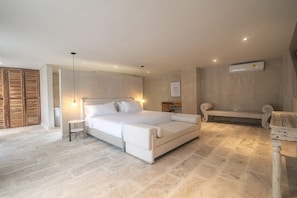Quarto com uma cama grande, mesas de cabeceira, escrivaninha, um banco e ar condicionado.