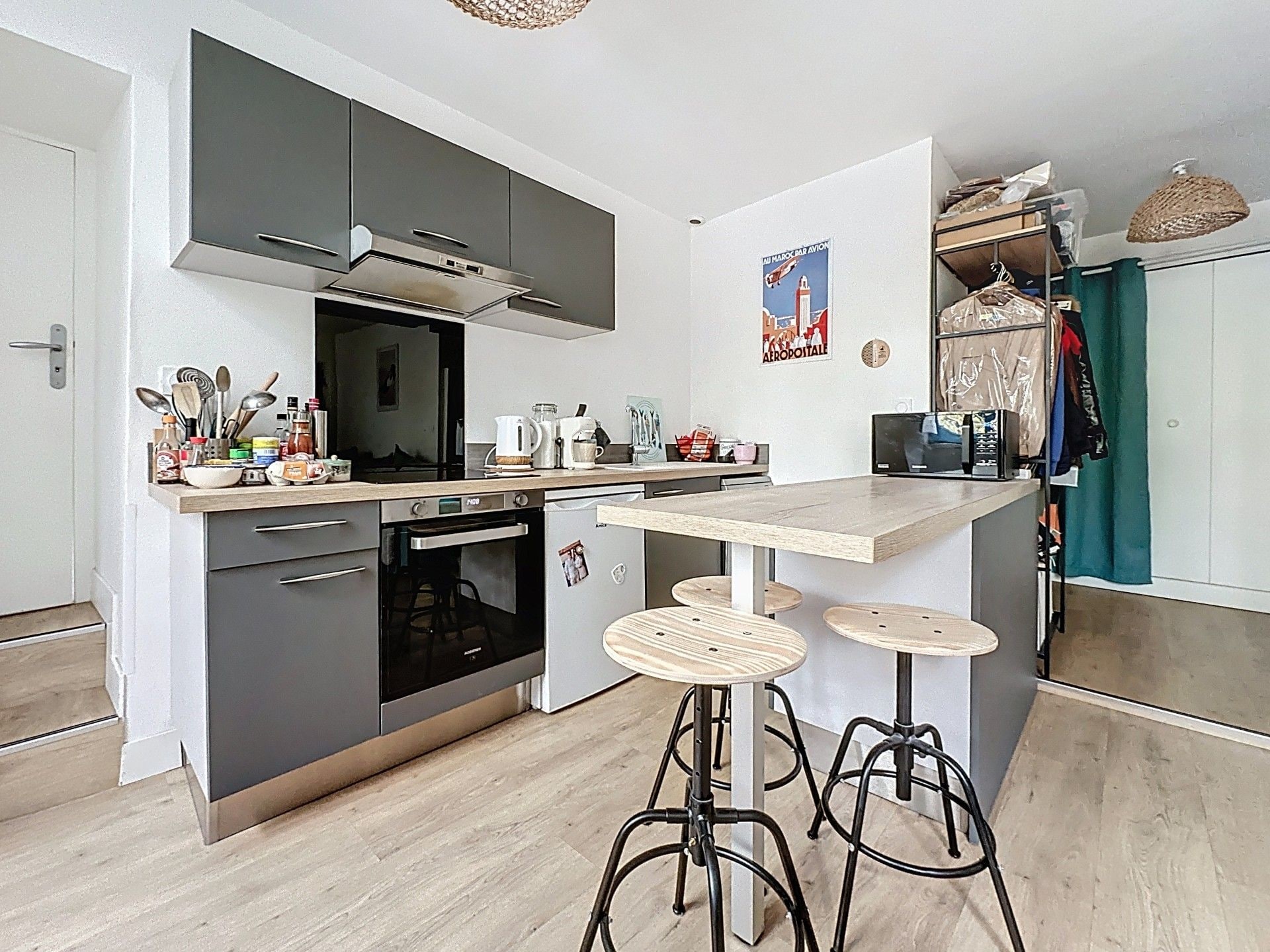 Cocina compacta con horno integrado, cafetera y taburetes de bar.