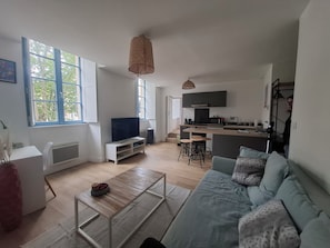 En moderne stue med sofa, sofabord og fjernsyn. Der er et køkkenområde med mikrobølgeovn og vask.