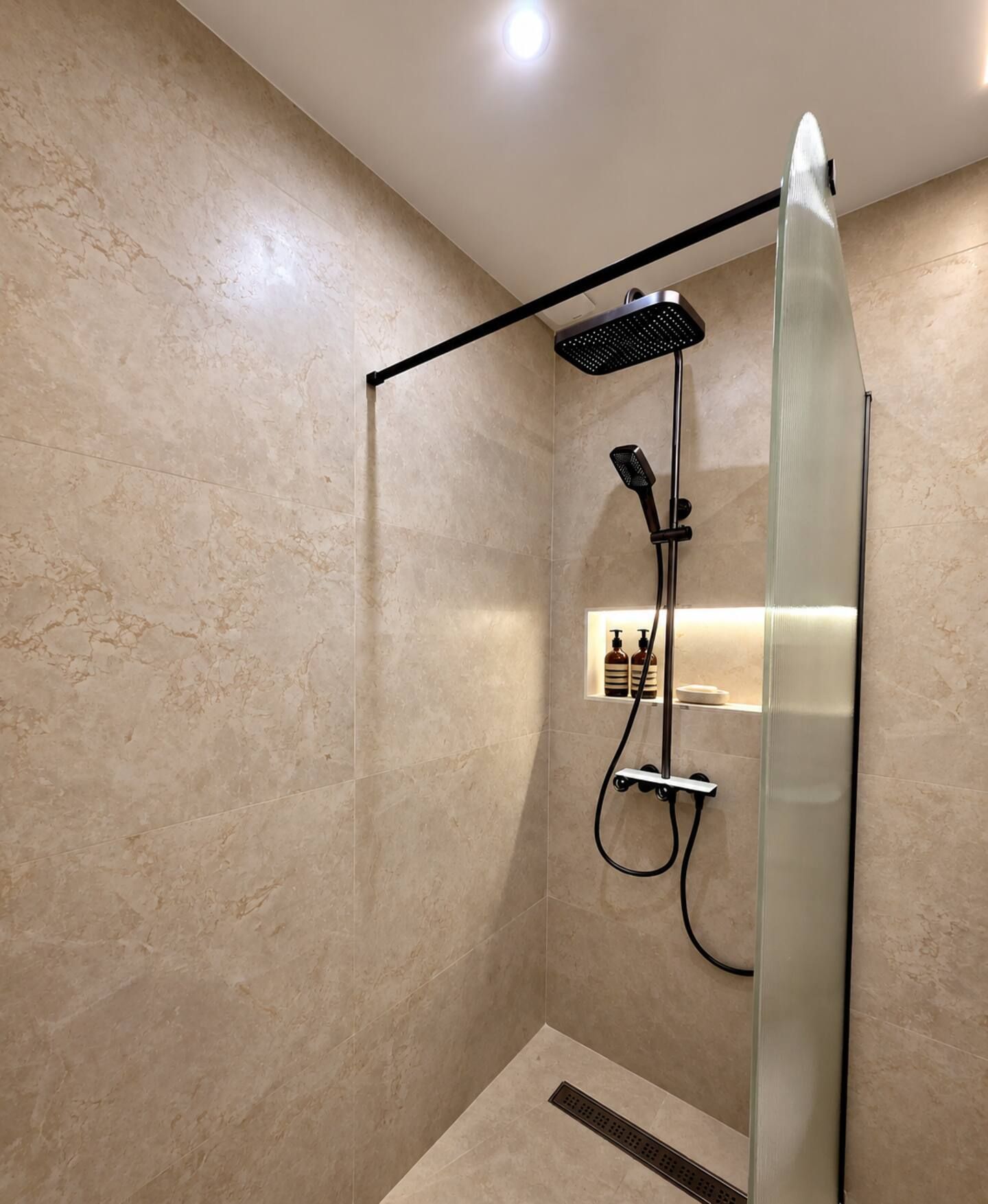 Une douche moderne dotée d’une porte en verre, d’un pommeau de douche à main et d’un panneau de commande fixé au mur.