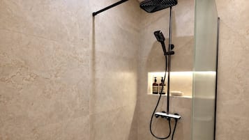 Une douche moderne dotée d’une porte en verre, d’un pommeau de douche à main et d’un panneau de commande fixé au mur.