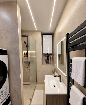 Une salle de bain moderne avec une douche à parois de verre, un lavabo blanc et un porte-serviettes noir.