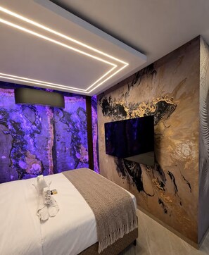 Un dormitorio moderno con cama, televisor de pantalla plana en la pared e iluminación ambiental.