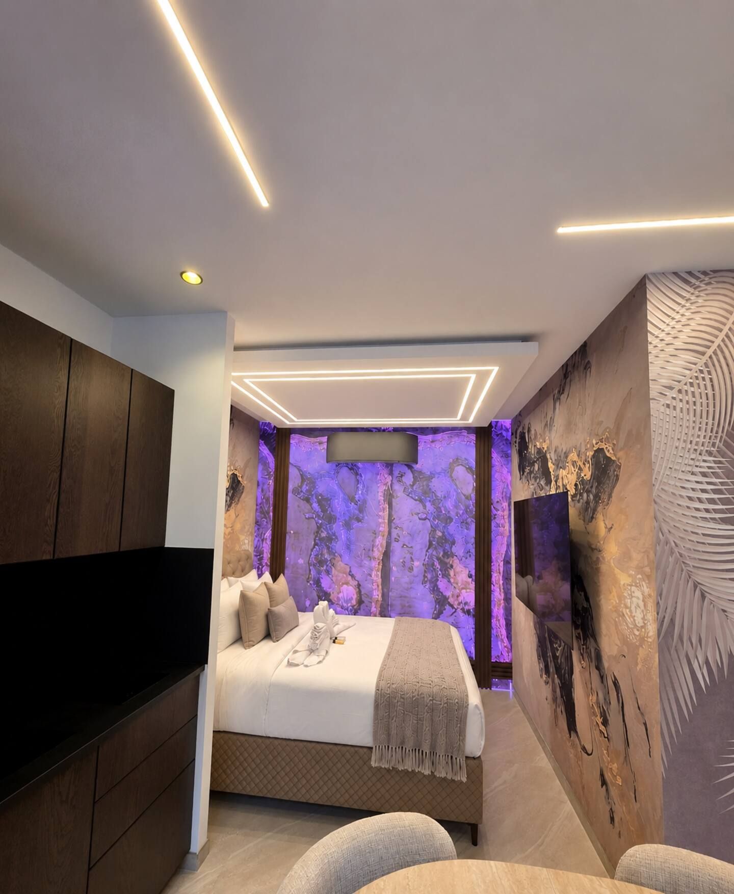Une chambre moderne avec un lit, un téléviseur à écran plat, une armoire en bois et un mur décoré d’œuvres d’art abstraites.